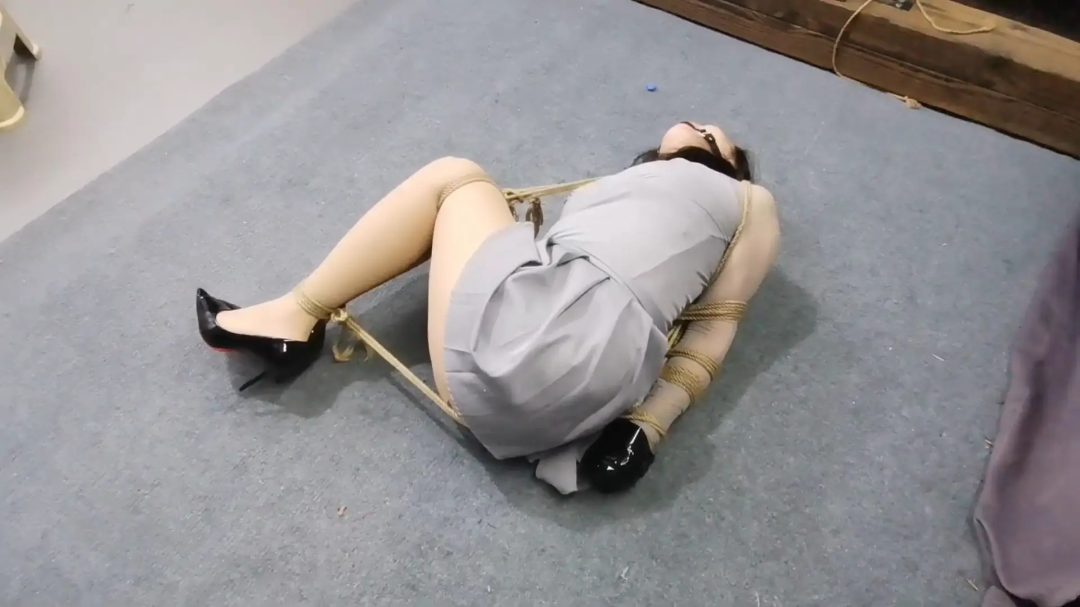 李然被直臂紧缚倒在地上，膝盖和脚踝紧缚让她无法逃脱，双手还被胶带缠绕，即使这样，她仍然奋力挣扎，只是徒劳无功罢了。